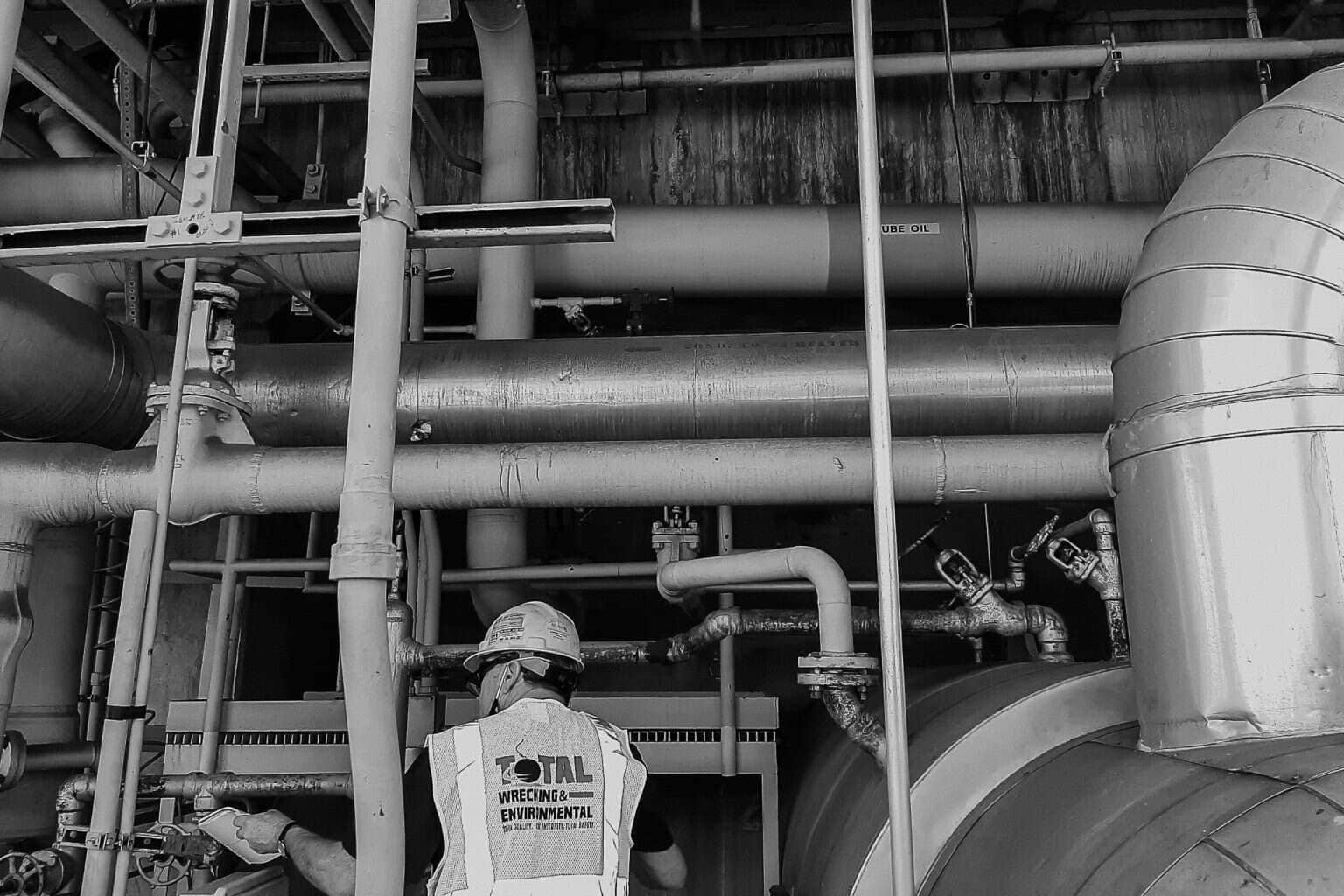 A Total Wrecking crew member in a hard hat surrounded by piping inside the McIntosh plant