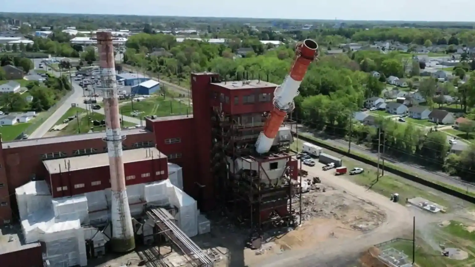 Aerial view of the McKee Run powerhouse in Dover, Delaware, as one of its stacks comes down, with homes beside the site