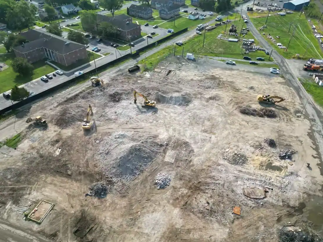 Aerial view of the cleared McKee Run lot in Dover during final grading, with excavators working and apartment buildings across the road